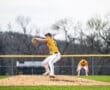 Baseball pitcher prepares to pitch from the mound during a game, with teammates in the background.