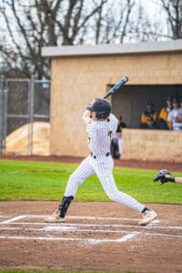 Young baseball player swinging a bat during a game, wearing a striped uniform and focused on hitting the ball.