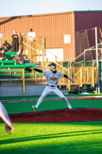 High school baseball player in a gray uniform pitching on a brightly colored field during a game.