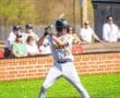 Young baseball player in action, poised at home plate, wearing a Tigers uniform with spectators in the background.