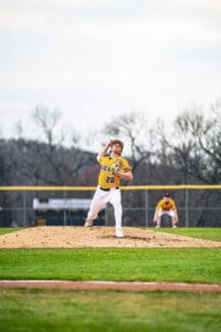 Young baseball pitcher in action on the mound, wearing a yellow jersey and showcasing throwing form during a game.