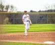 Baseball player in a striped Tigers uniform stands on the field, ready for action under a clear sky.