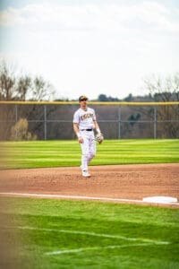 Baseball player in a striped Tigers uniform stands on the field, ready for action under a clear sky.