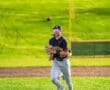 High school baseball player running on the field, wearing a uniform and sunglasses at an athletic complex.