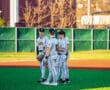 Baseball players in gray uniforms gather on a field, discussing strategy under a clear sky.