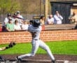 Youth baseball player swings bat, aiming to hit the ball, with spectators watching in the background on a sunny day.