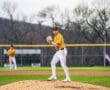 High school pitcher on the mound, wearing a yellow jersey, preparing to pitch during a baseball game.