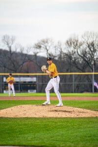 High school pitcher on the mound, wearing a yellow jersey, preparing to pitch during a baseball game.