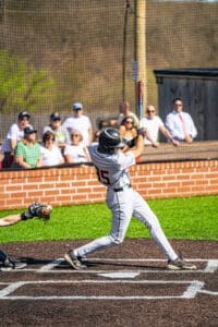 Youth baseball player in action, swinging a bat during a game with spectators in the background. Perfect spring day.
