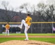 Baseball pitcher in action, wearing a yellow jersey and white pants, preparing to throw on the mound during a game.