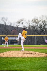 Baseball pitcher in action, wearing a yellow jersey and white pants, preparing to throw on the mound during a game.