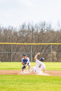 Two young baseball players in action on the field, one sliding into second base while the other prepares to tag him.
