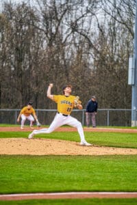 High school baseball pitcher in action, wearing a yellow Tigers uniform, on the mound during a game.