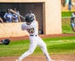 A baseball player in a striped uniform swings a bat at home plate during a game, with spectators in the background.