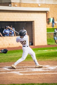 A baseball player in a striped uniform swings a bat at home plate during a game, with spectators in the background.