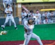 A baseball player swings at a pitch on a colorful field, with teammates cheering from the dugout behind him.