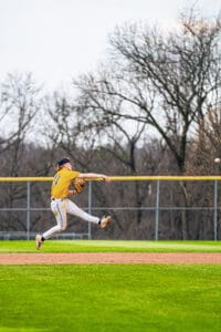 Youth baseball player in yellow jersey fields and throws a ball during a game on a grassy field.