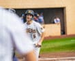A young baseball player in a striped uniform smiles while on the field, showcasing team spirit and camaraderie.
