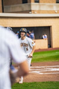 A young baseball player in a striped uniform smiles while on the field, showcasing team spirit and camaraderie.