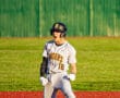 Excited baseball player in gray uniform celebrating on the field after a significant play, kneeling on the base.