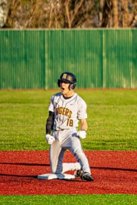 Excited baseball player in gray uniform celebrating on the field after a significant play, kneeling on the base.