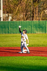 Baseball player celebrating a hit on a vibrant field, wearing team jersey and cap, pointing upward with excitement.