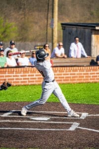 A young baseball player swings a bat during a game, with spectators watching in the background on a sunny day.