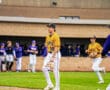 Baseball player in yellow jersey walks on field, teammates in background. Action shot from a competitive game.