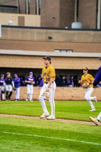 Baseball player in yellow jersey walks on field, teammates in background. Action shot from a competitive game.