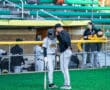 Coach advises young baseball player at the field, with teammates in the background watching the action.