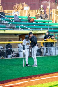 Coach advises young baseball player at the field, with teammates in the background watching the action.