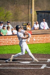A baseball player swings at a pitch during a game, with spectators in the background cheering on the action.