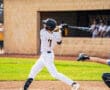 Young baseball player in striped uniform swings bat during a game, capturing dynamic athletic energy on the field.