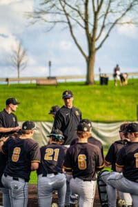 Baseball coach discussing strategies with players during practice on a sunny day at the field. Team in black uniforms.
