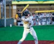 Baseball player in action, preparing to swing bat at home plate during a game, with teammates in the background.