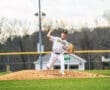 High school baseball pitcher on the mound winding up for a pitch during an afternoon game. Clear skies in the background.