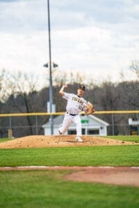 High school baseball pitcher on the mound winding up for a pitch during an afternoon game. Clear skies in the background.