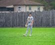 A young baseball player in a gray uniform stands on a green field, ready to catch the ball during a game.