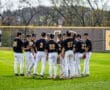 A youth baseball team in black and white uniforms huddles together on a sunny field, discussing strategy and teamwork.