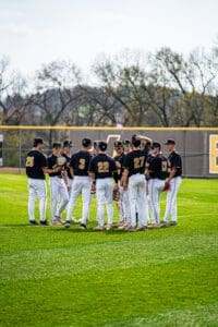 A youth baseball team in black and white uniforms huddles together on a sunny field, discussing strategy and teamwork.