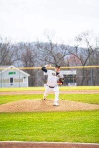 Baseball pitcher in striped uniform winds up on the mound, showcasing athleticism on a sunny day at the ballpark.