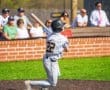 Young baseball player in gray uniform swings bat during sunny game, with spectators in background enjoying the match.