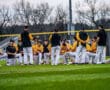 Baseball team gathers for a motivational talk on the field, wearing yellow jerseys and black jackets during practice.