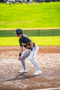 Baseball player in a black jersey crouching at base on a sunny field, ready for action during a game.