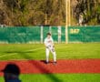 Baseball player in white uniform on the field, ready to play, with a vibrant green and red turf background.