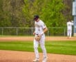 High school baseball player in striped uniform walks the infield, ready for the next play on a sunny day.