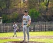 Player in gray baseball uniform stands on the pitcher's mound, focused on the game during a vibrant outdoor match.