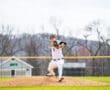 A young baseball pitcher in a striped uniform winds up on the mound during a sunny day at the ballpark.