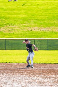 Young baseball player in action, throwing a ball on a sunny day at the field, showcasing athleticism and focus.