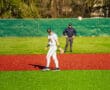 Baseball player fielding on a vibrant turf, with an umpire observing in the background on a sunny day.